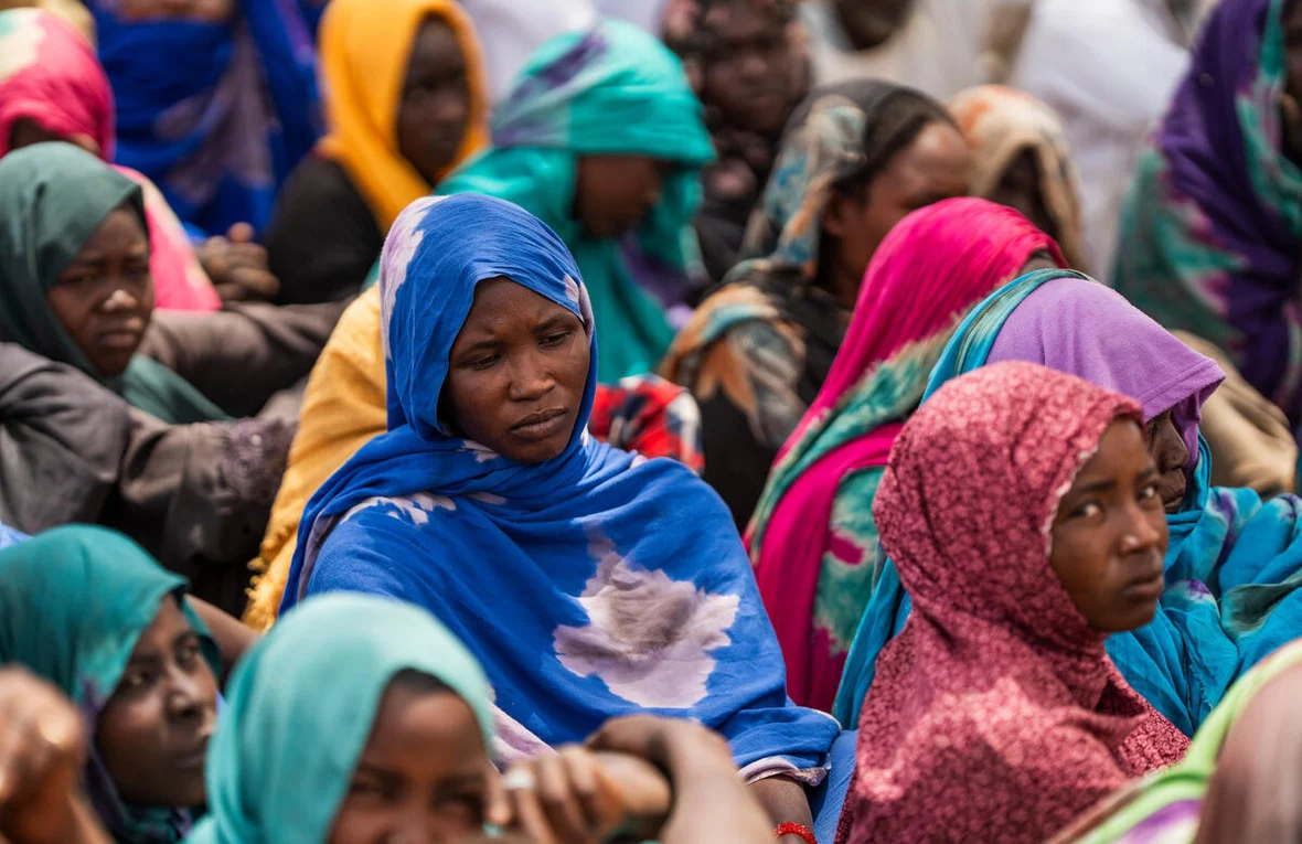 Un grand groupe de réfugiées soudanaises vêtues de coiffes et de châles colorés se tient debout dans un camp provisoire au Tchad.
