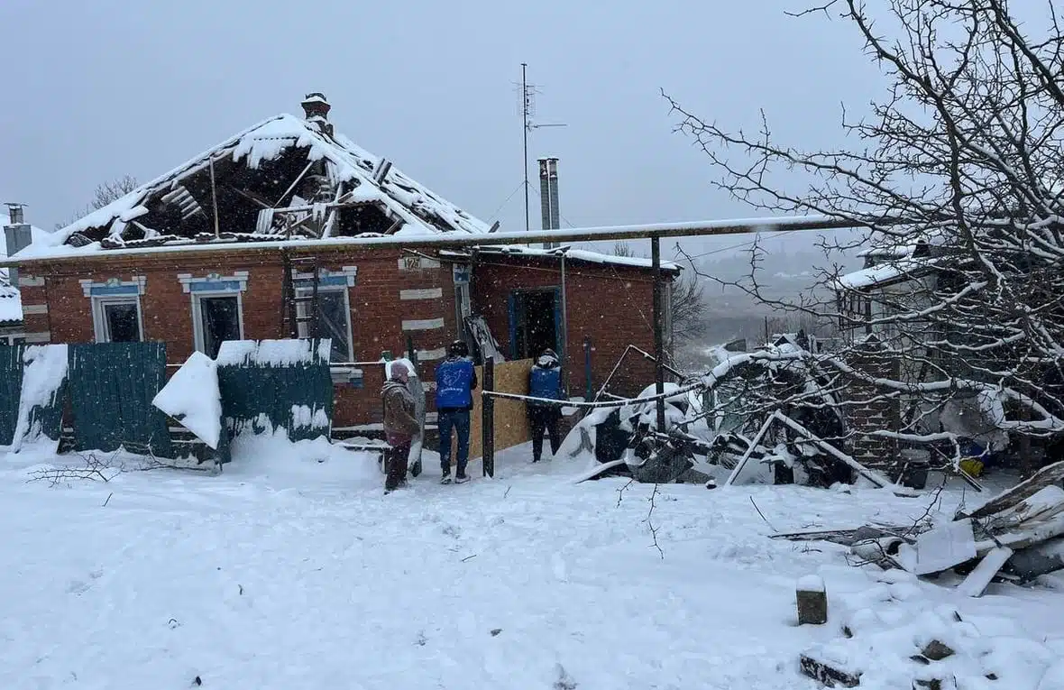 A group of NGO Proliska volunteers are visiting a heavily damaged one-storey house covered in snow.