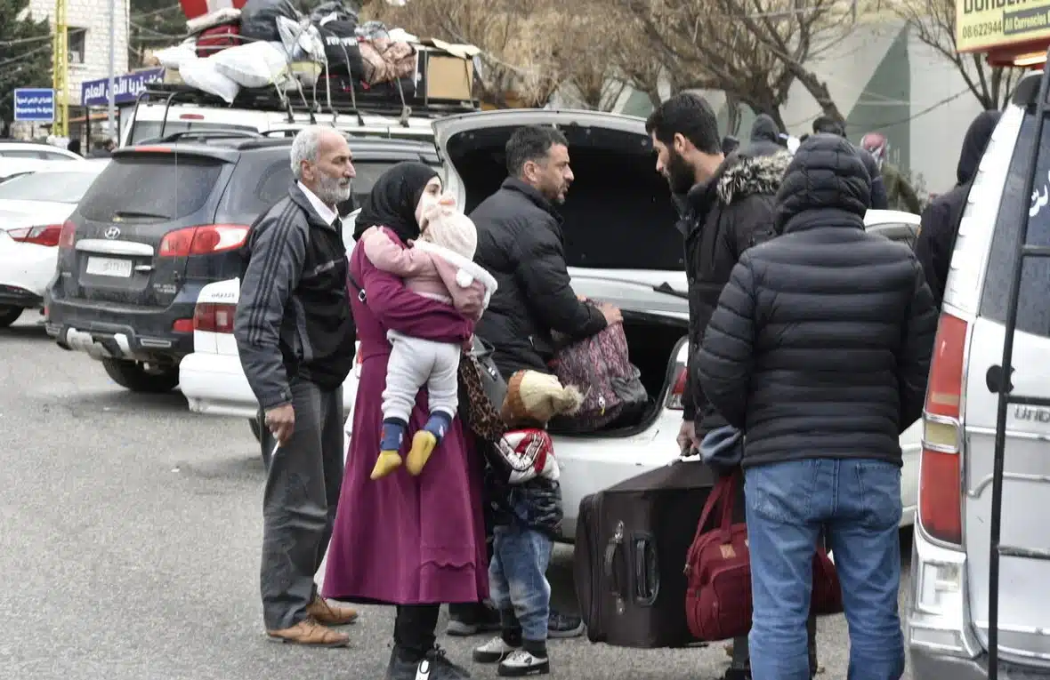 Une famille, composée de quatre hommes et d'une femme avec deux jeunes enfants, est photographiée avec ses bagages près d'une voiture dont le coffre est ouvert.