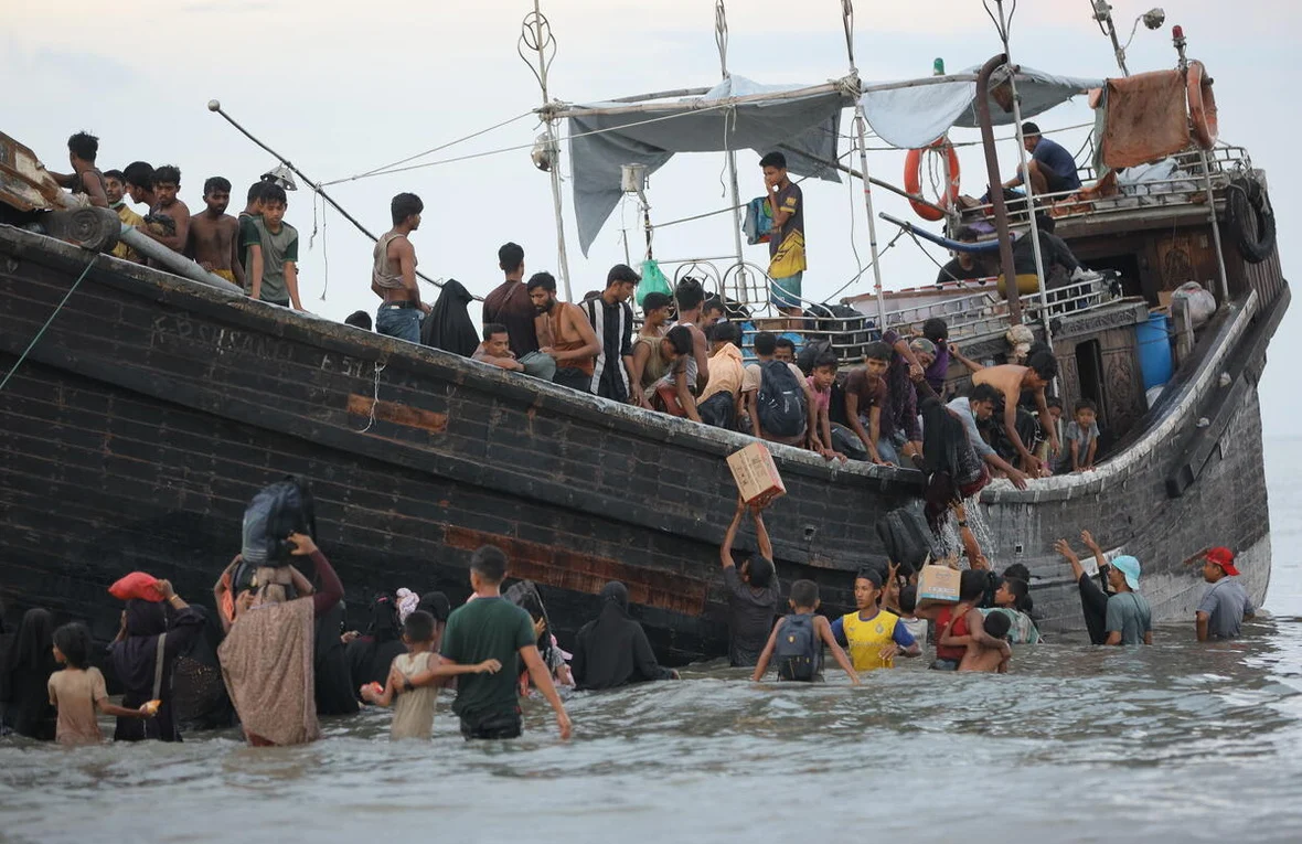 People can be seen disembarking from a dingy as some are waste deep in sea waters and others unloading their meager belongings from the boat.