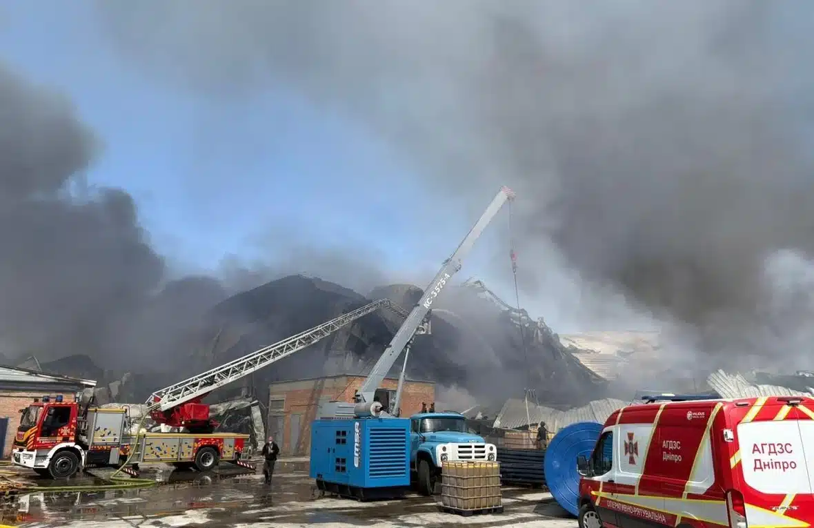 Emergency crews and a crane respond to a destroyed warehouse engulfed in black smoke in Dnipro, Ukraine.