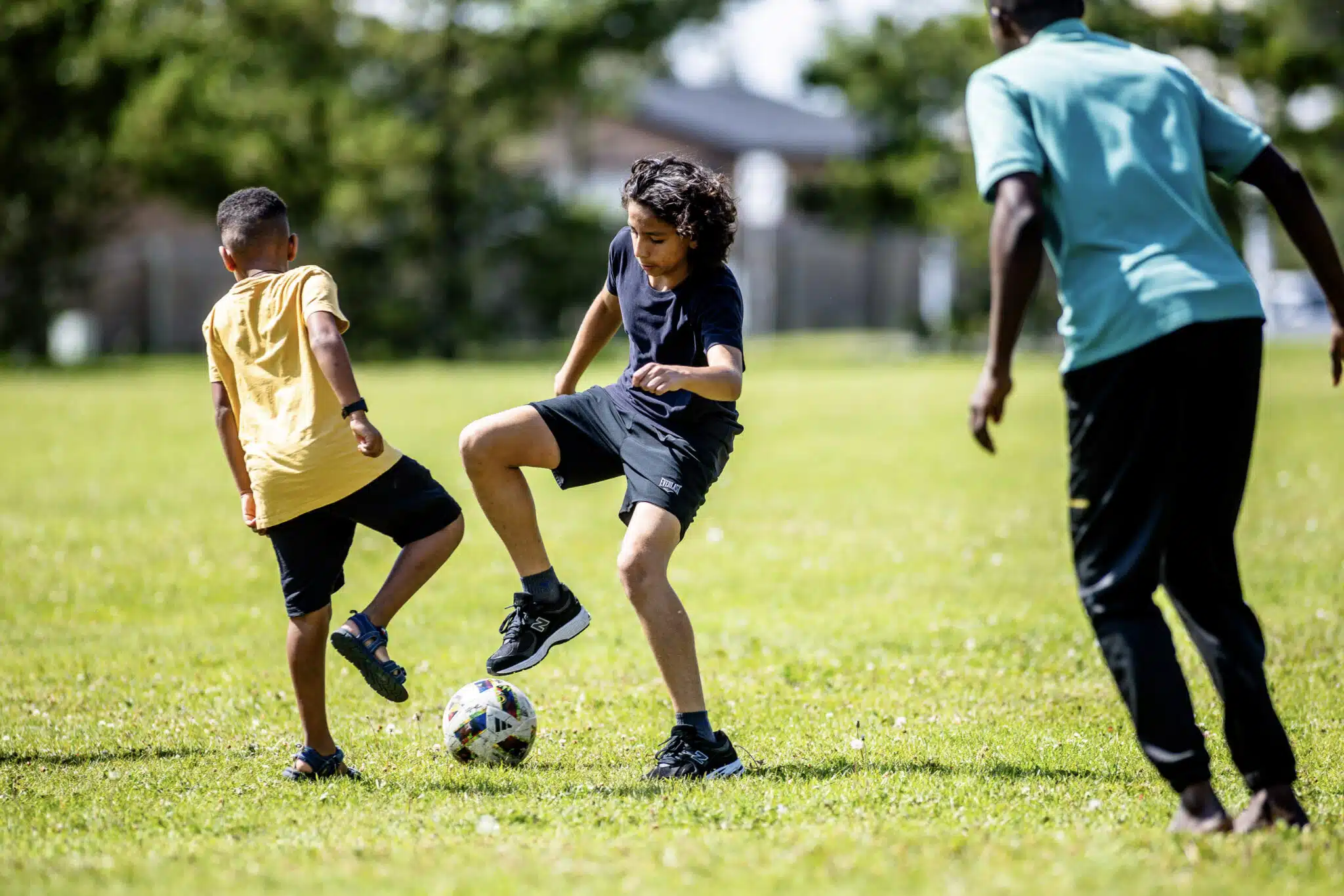 On voit trois garçons jouer au football sur un terrain vert