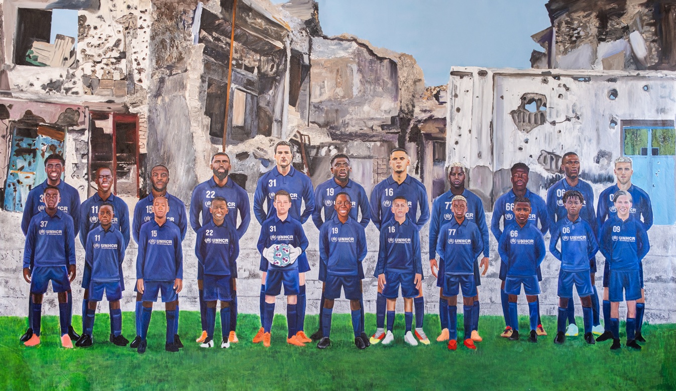 Eleven soccer players dressed in blue soccer jerseys with the UNHCR logo on it stand on a pitch with their childhood likeness standing in front of them while behind them are scenes of destruction caused by war.