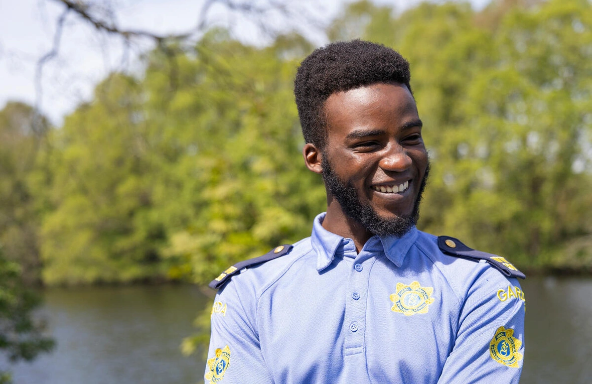 Outdoor portrait of uniformed personnel smiling at the camera with natural greenery and water visible in the background.