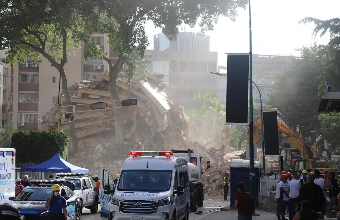 Ambulances and heavy construction equipment can be seen parked on a street next to a collapsed building.