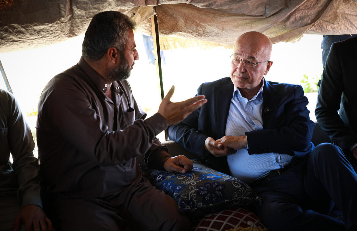UN High Commissioner for Refugees Barham Salih speaks to a middle-aged man while sitting inside a tent.