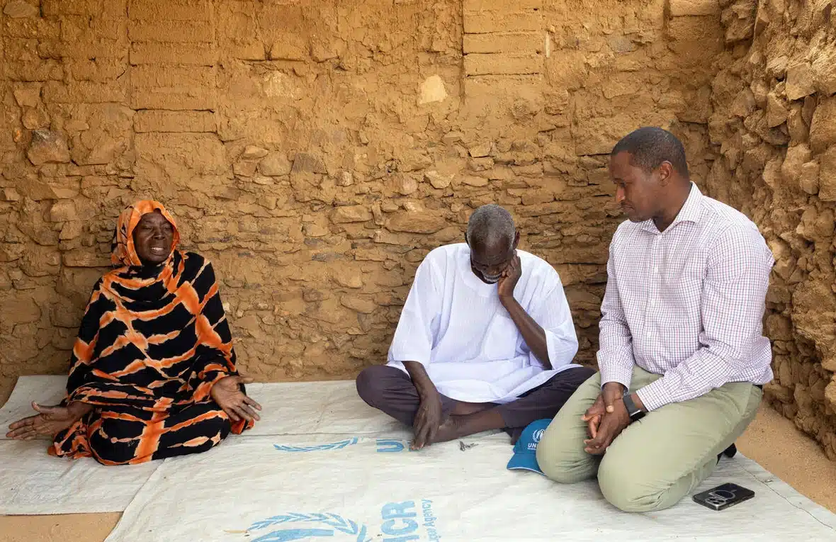UNHCR Regional Refugee Coordinator for the Sudan situation, Mamadou Dian Balde sits on his knees on a white UNHCR tarp on an earthen floor inside a mud and stone hut listening to the harrowing story of Sudanese refugees Leila and Ousmane at the Kouchaguine Moura site, eastern Chad.