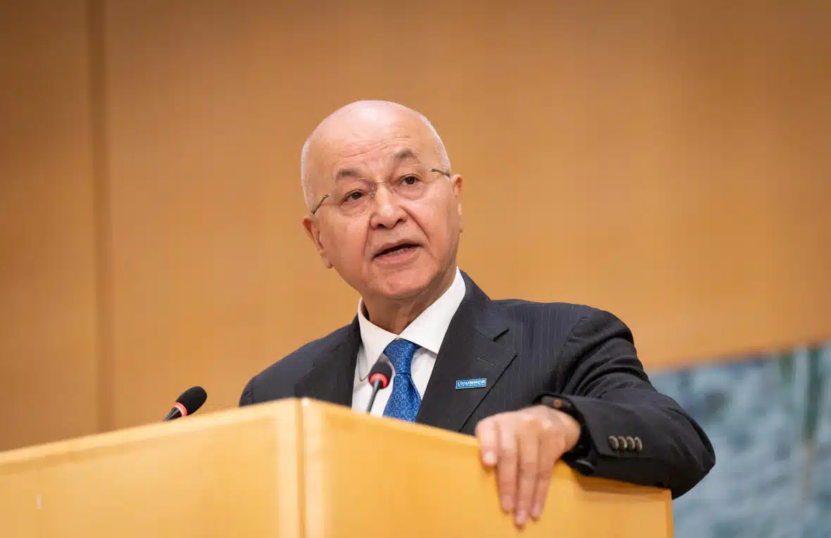 A middle-aged man dressed in a dark suit is seen speaking from a podium.